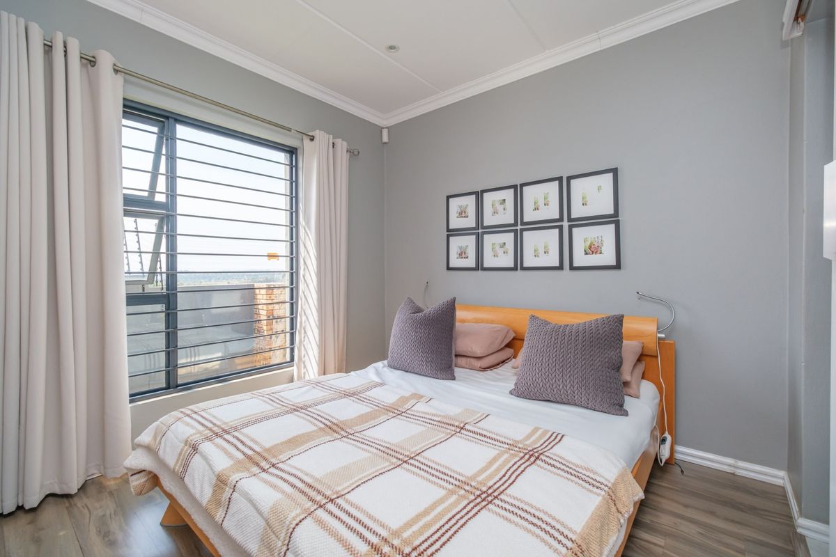 A well-maintained bedroom featuring modern laminate flooring, neutral grey walls, and an aluminium window with integrated security bars.