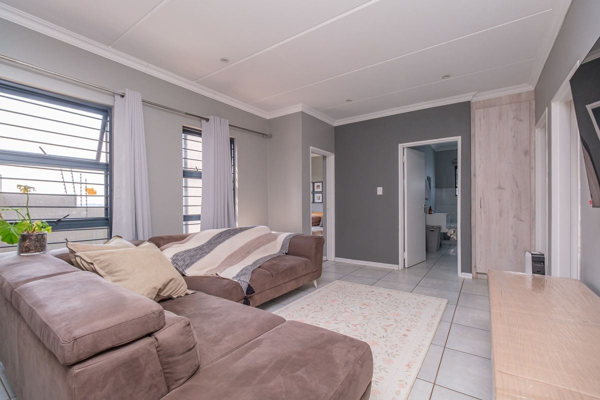 A well-maintained living room featuring tiled flooring, recessed ceiling lights, and a built-in cupboard, with direct access to adjacent rooms.