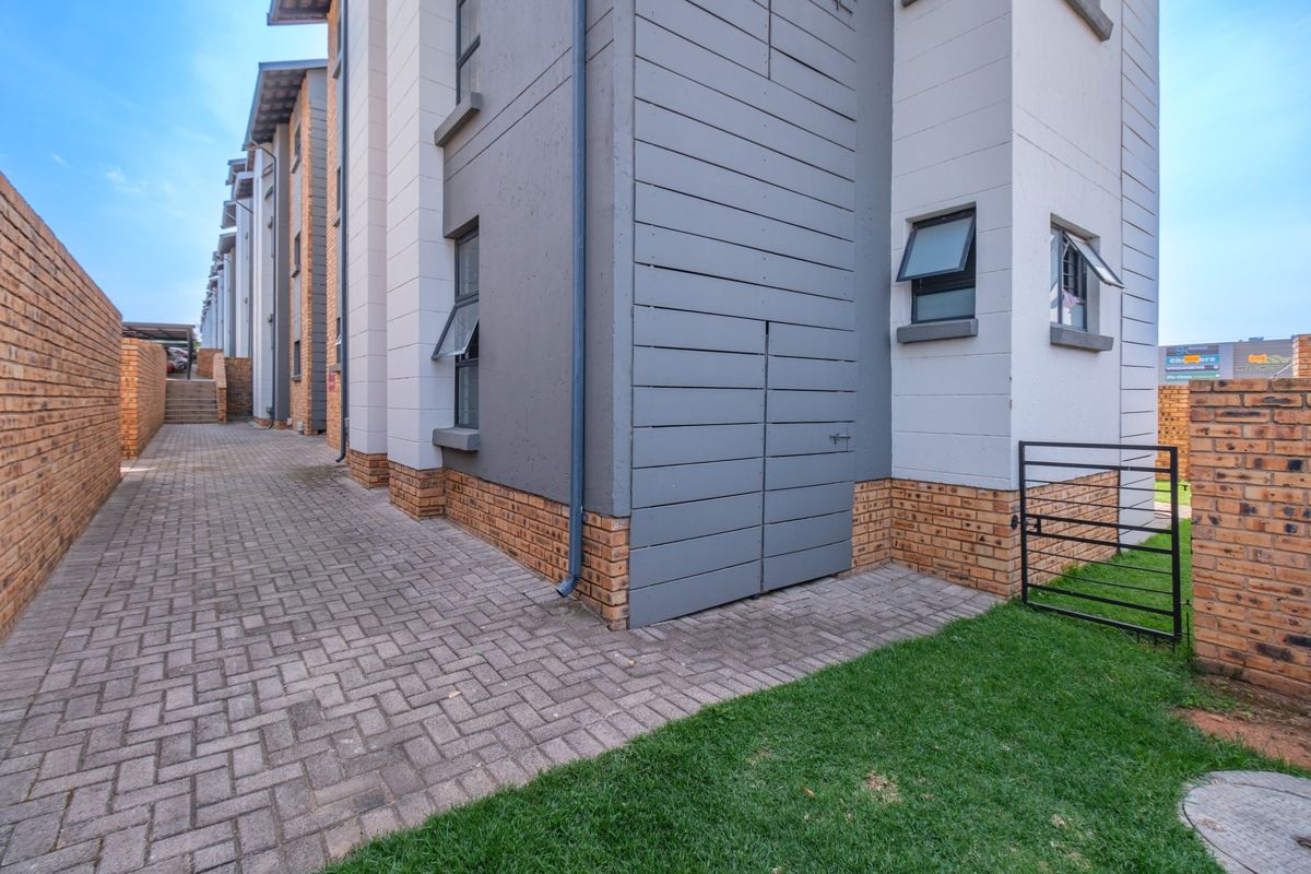 A view of the rear exterior of the flat, featuring brick paving, a brick boundary wall, and modern grey timber cladding accents.