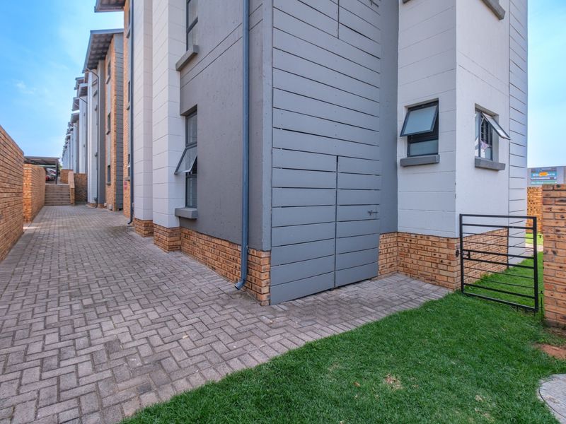A view of the rear exterior of the flat, featuring brick paving, a brick boundary wall, and modern grey timber cladding accents.