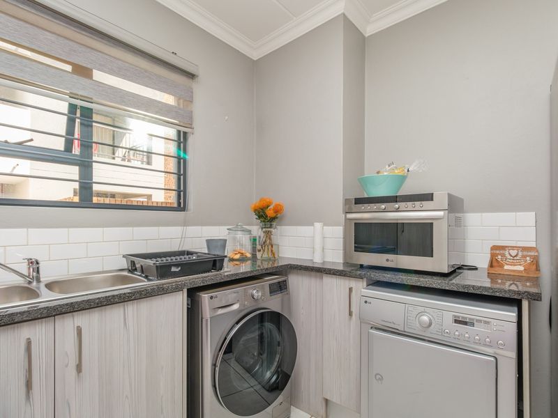 A well-maintained laundry area featuring granite countertops, subway tile backsplash, built-in cabinetry, and a stainless steel sink with a mixer tap.