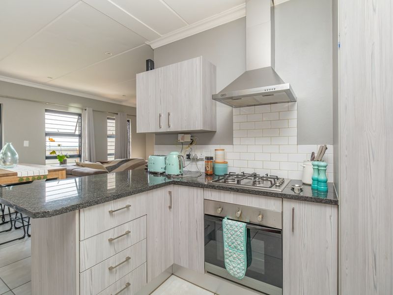 Modern open-plan kitchen featuring light wood-grain cabinetry, granite countertops, a gas hob, and a subway tile backsplash, seamlessly flowing into the living area.