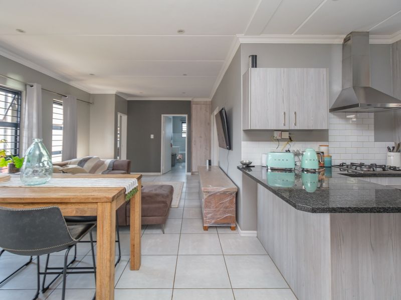 Open-plan living area featuring a modern kitchen with granite countertops, gas hob, stainless steel extractor, and tiled flooring throughout the combined space.