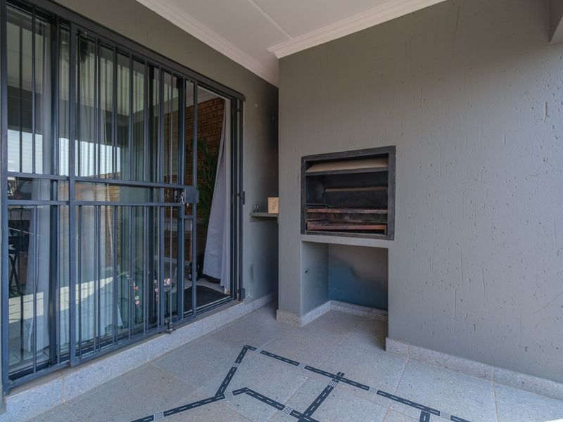 Covered patio area featuring a built-in braai, tiled flooring, and a secure sliding door entrance to the interior.