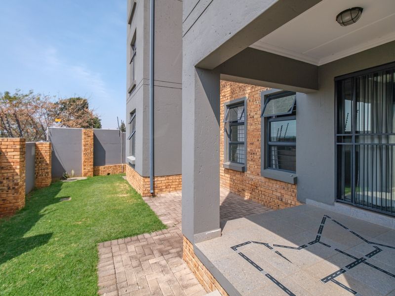 A covered patio area with paved flooring, overlooking a small private garden enclosed by brick boundary walls and electric fencing.