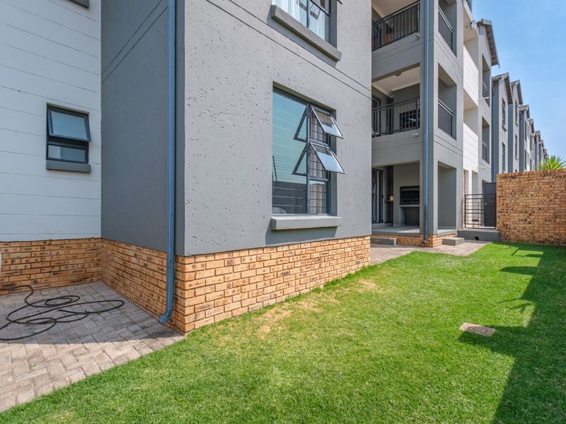 Rear view of a modern flat featuring a private garden, paved patio area with a built-in braai, and access to upper-level balconies.