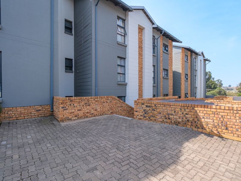 Exterior view of a modern apartment complex featuring face brick retaining walls and paved driveway access.