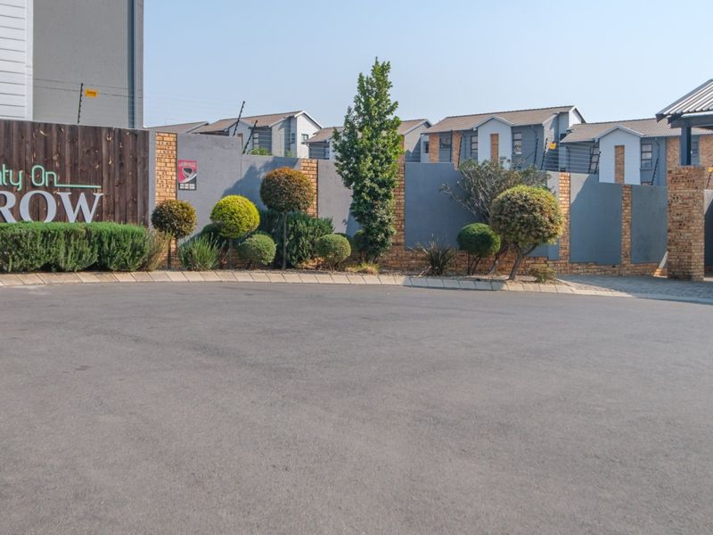 The entrance to the Twenty On Furrow complex, featuring a paved driveway, secure perimeter wall with electric fencing, and manicured garden landscaping.