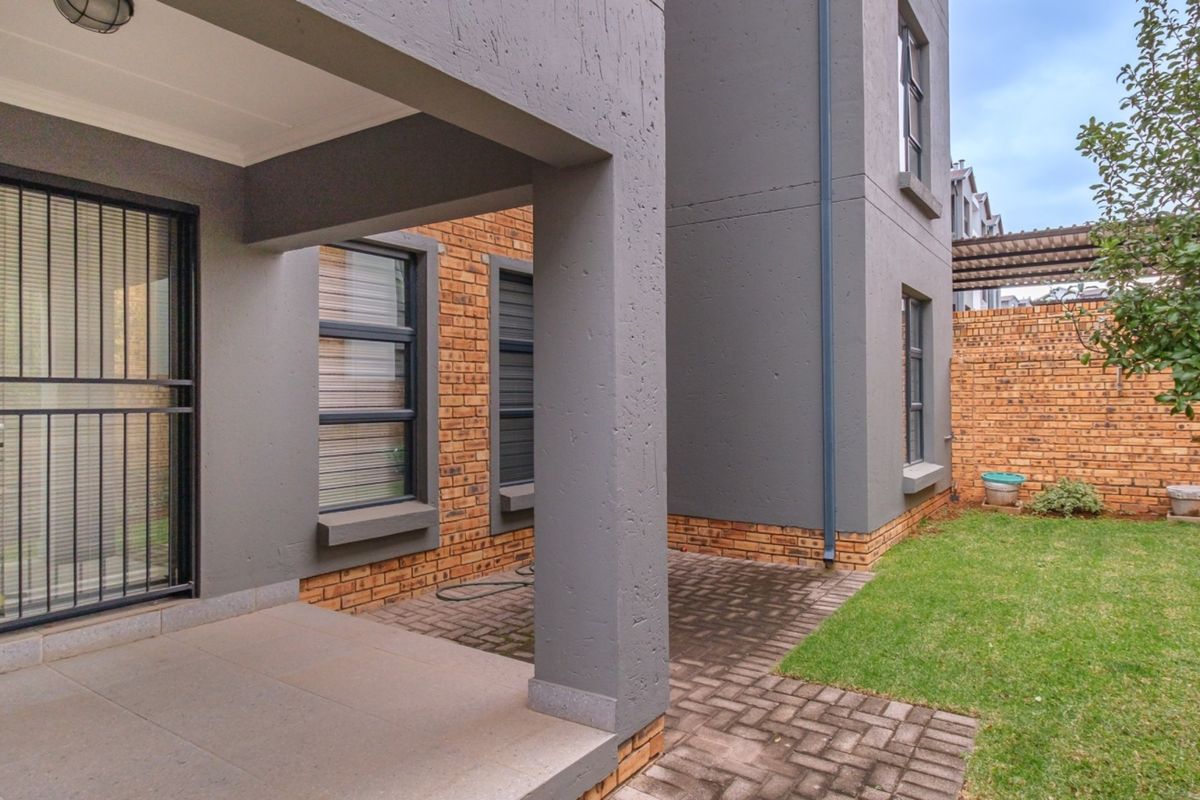 A well-maintained rear exterior featuring a covered patio, paved walkway, and a private garden enclosed by a brick boundary wall.