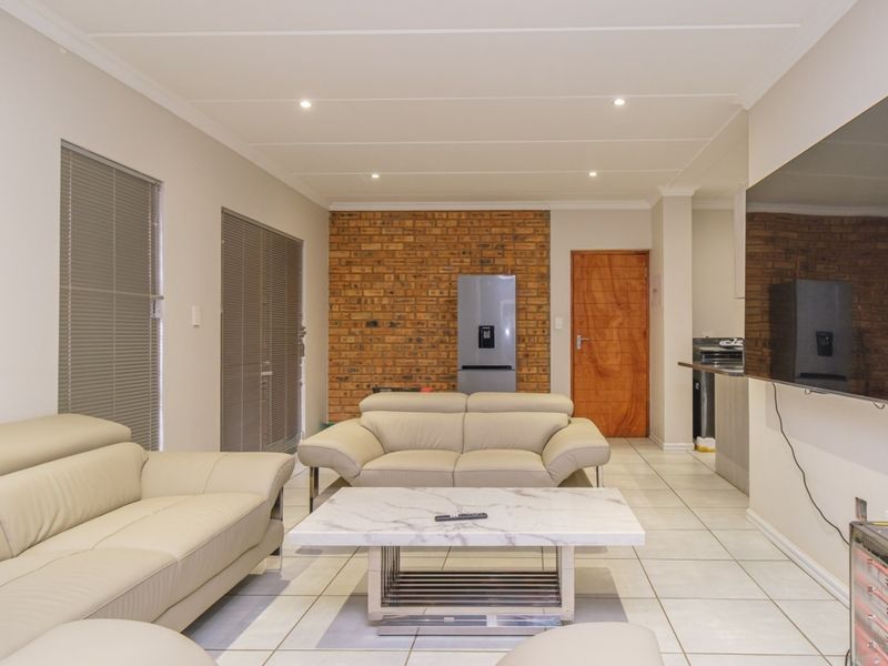 Spacious open-plan living area featuring a striking exposed brick wall, neutral tiled flooring, and recessed downlighting, creating a bright and functional living space.