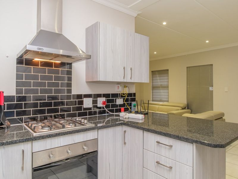 Modern open-plan kitchen featuring granite countertops, light wood-grain cabinetry, a gas hob, and a stylish black subway tile backsplash, flowing into the living area.