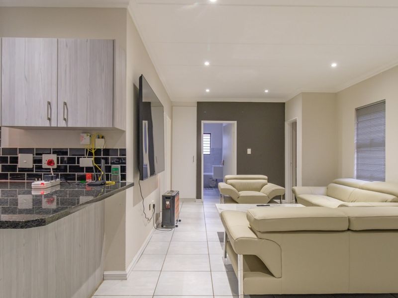 An open-plan living and kitchen area featuring modern cabinetry, granite countertops, a subway tile backsplash, and neutral tiled flooring throughout.