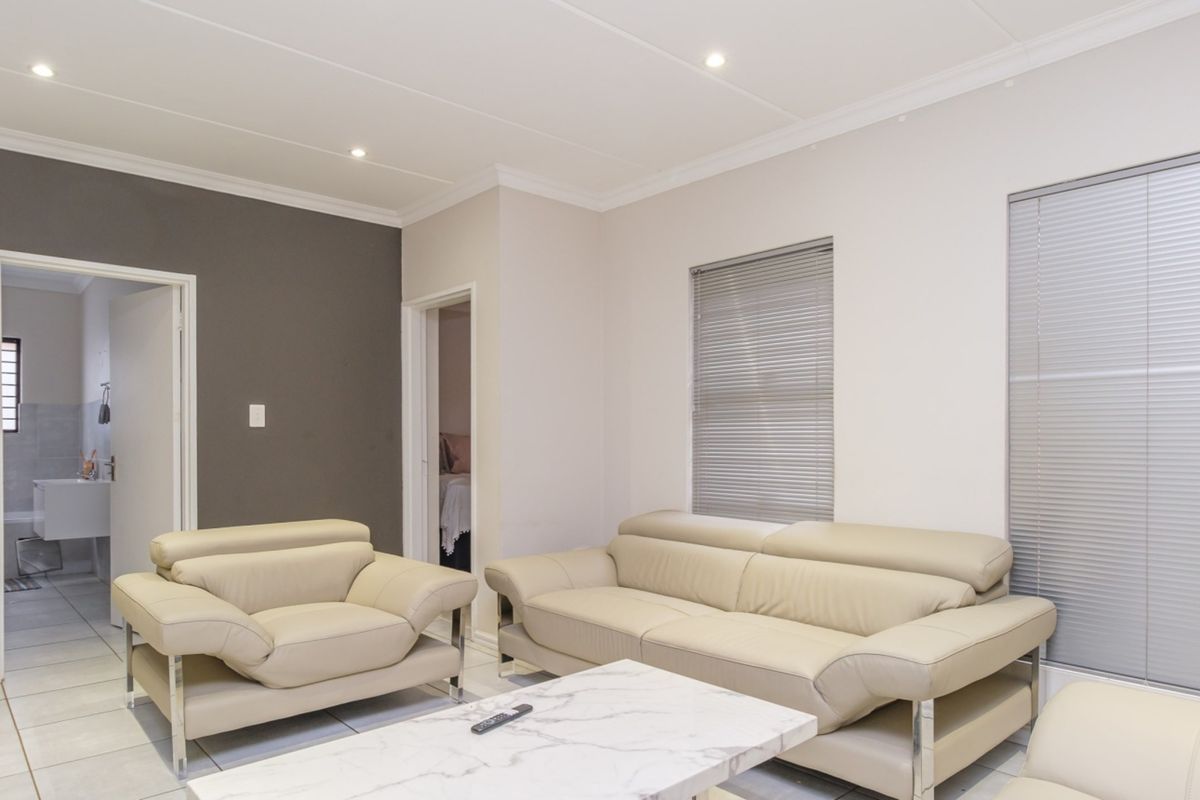 A bright living room featuring tiled flooring, recessed downlighting, and venetian blinds, with neutral wall tones and a coved ceiling.