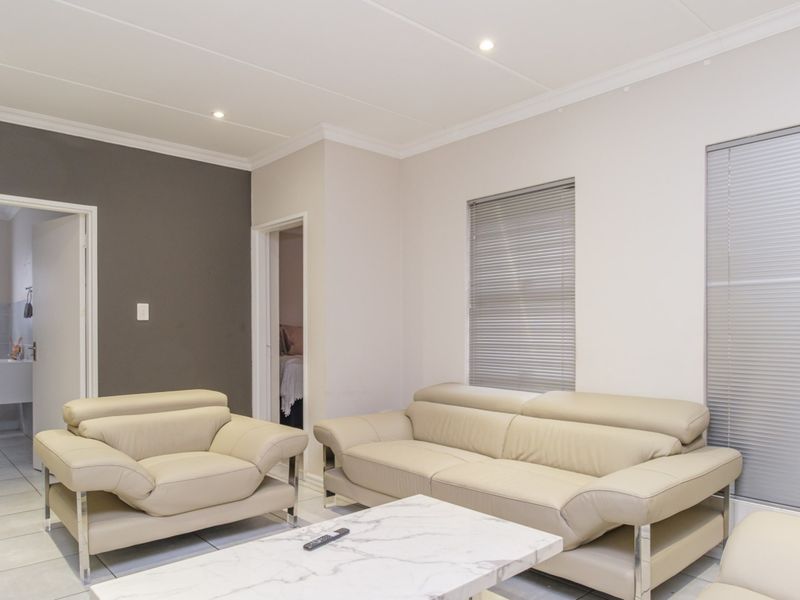 A bright living room featuring tiled flooring, recessed downlighting, and venetian blinds, with neutral wall tones and a coved ceiling.