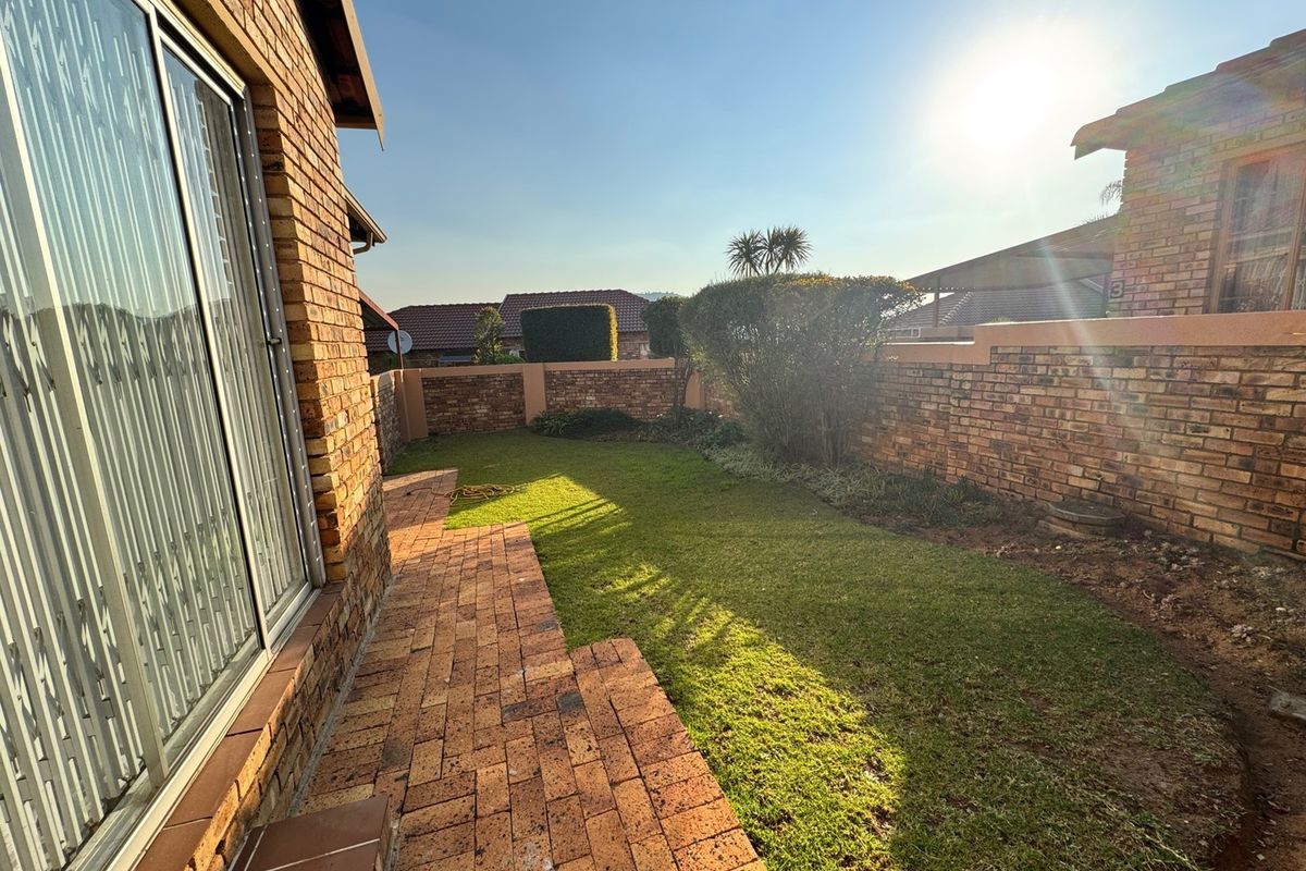 A private rear garden featuring a paved walkway, established lawn, and face brick boundary walls, accessible via a sliding glass door.