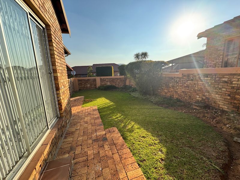 A private rear garden featuring a paved walkway, established lawn, and face brick boundary walls, accessible via a sliding glass door.