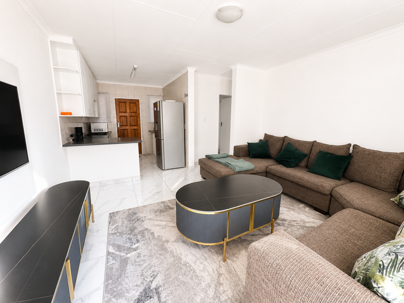 A bright open-plan living and kitchen area featuring modern tiled flooring, neutral walls, and functional built-in kitchen cabinetry.