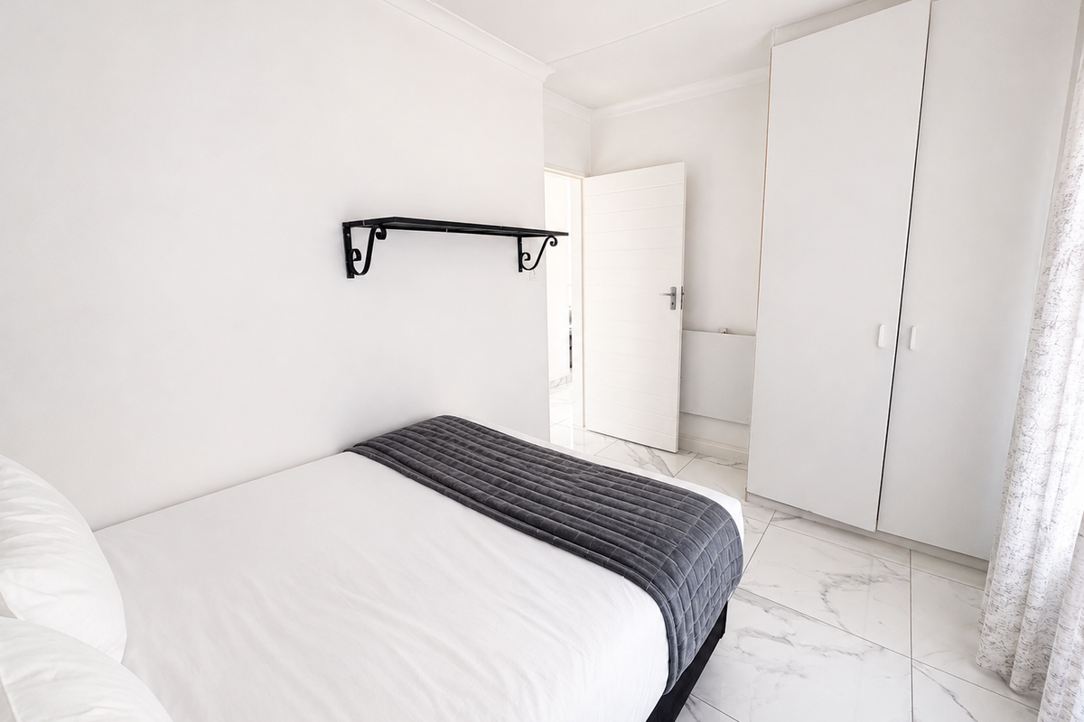 A bright bedroom featuring white built-in wardrobes, marble-effect floor tiles, and a clean, minimalist aesthetic.
