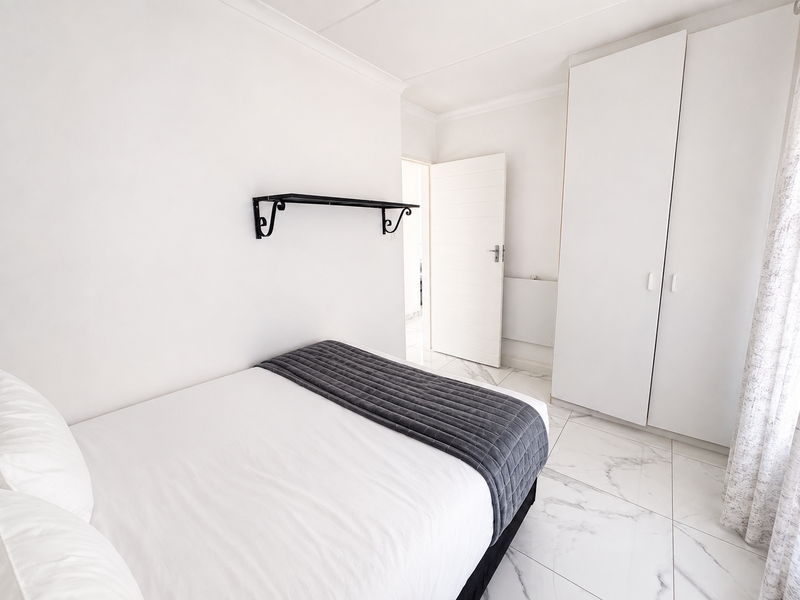 A bright bedroom featuring white built-in wardrobes, marble-effect floor tiles, and a clean, minimalist aesthetic.