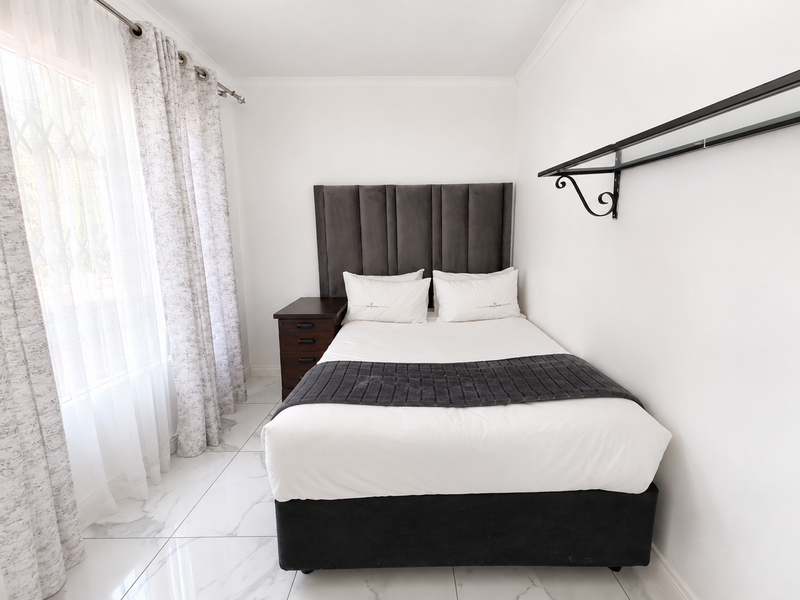 A bright and clean bedroom featuring modern white tiled flooring, neutral walls, and a wall-mounted display shelf.