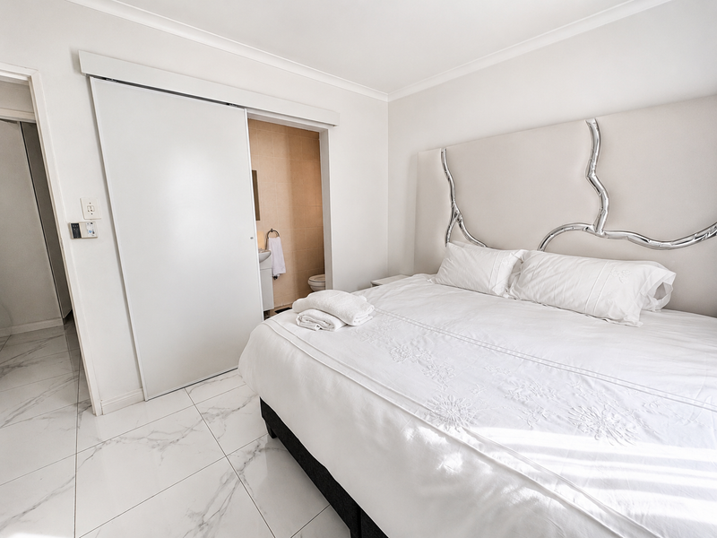 A bright bedroom featuring modern marble-look floor tiles, a sliding door leading to an en-suite bathroom, and neutral finishes throughout.