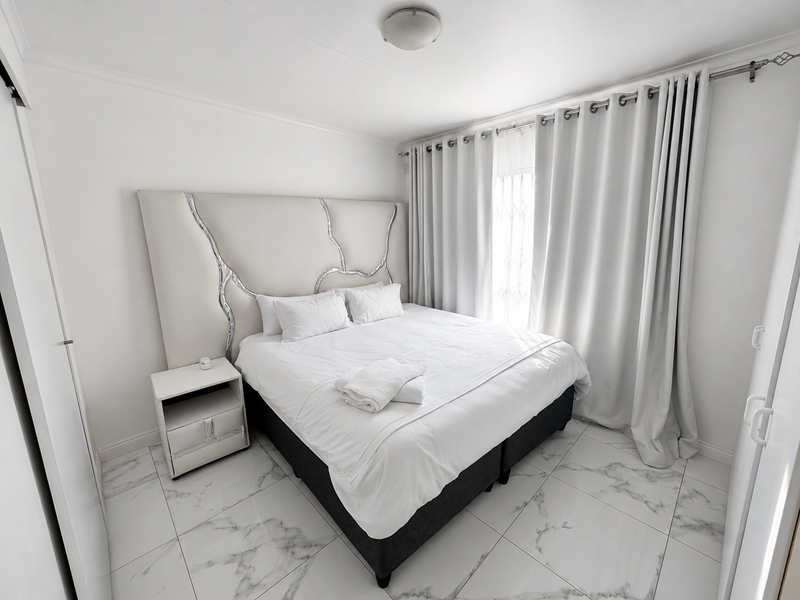 A bright and modern bedroom featuring marble-look floor tiles, a built-in wardrobe, and neutral finishes, creating a clean and contemporary living space.