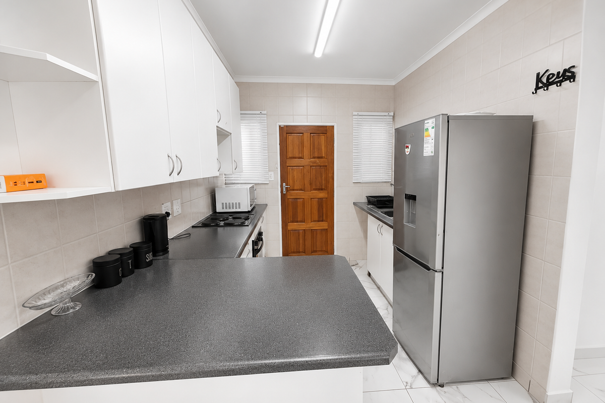 A functional kitchen featuring white cabinetry, dark laminate countertops, tiled backsplash, and tiled flooring, providing a clean and practical workspace.