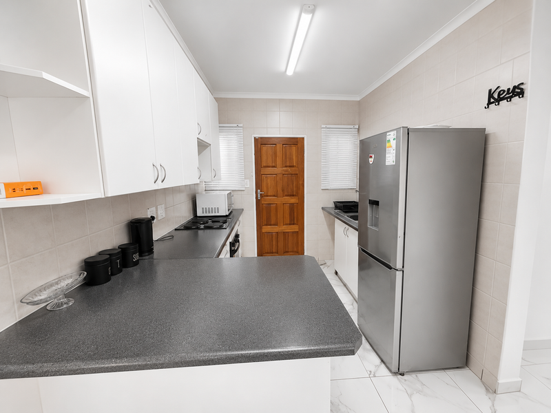 A functional kitchen featuring white cabinetry, dark laminate countertops, tiled backsplash, and tiled flooring, providing a clean and practical workspace.