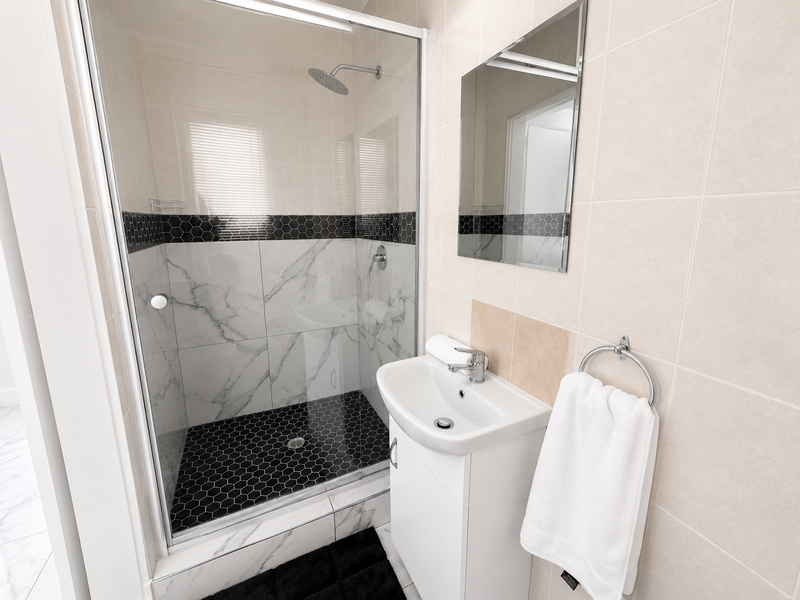 A modern bathroom featuring a glass-enclosed shower with rain shower head, vanity basin, and stylish contrasting hexagonal tile accents.