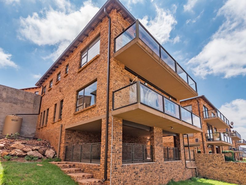 Rear view of a multi-story face brick cluster home featuring stacked balconies with glass balustrades and a ground-level covered patio area.