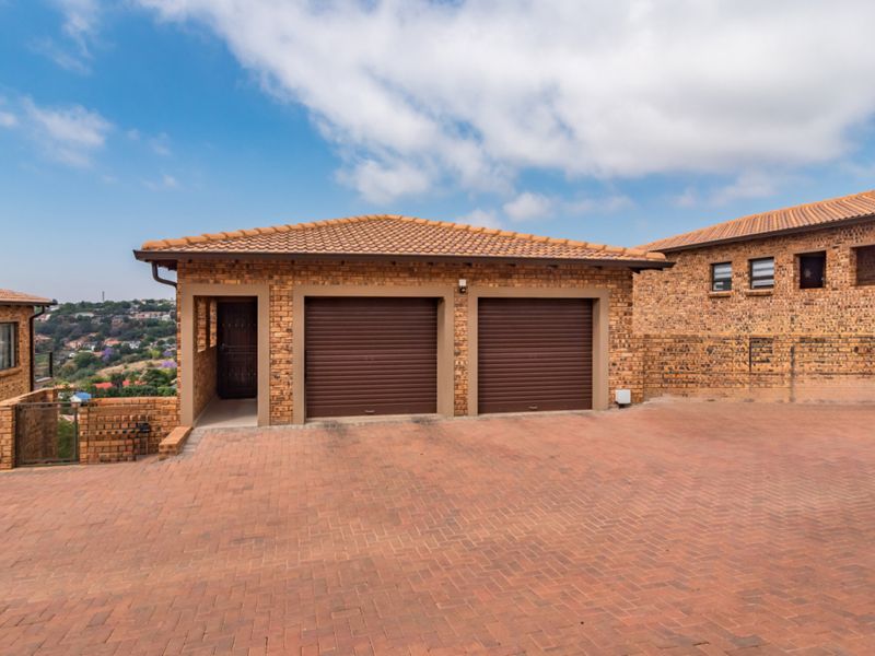 A well-maintained double garage with brick exterior, tiled roof, and paved driveway in a cluster property setting.