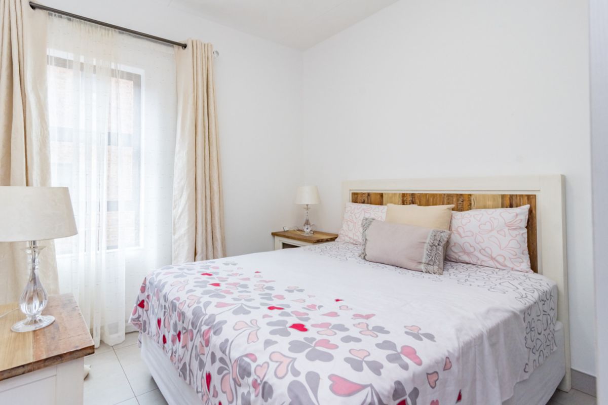 A bright and well-maintained bedroom featuring neutral walls, tiled flooring, and a window with fitted curtain rods.
