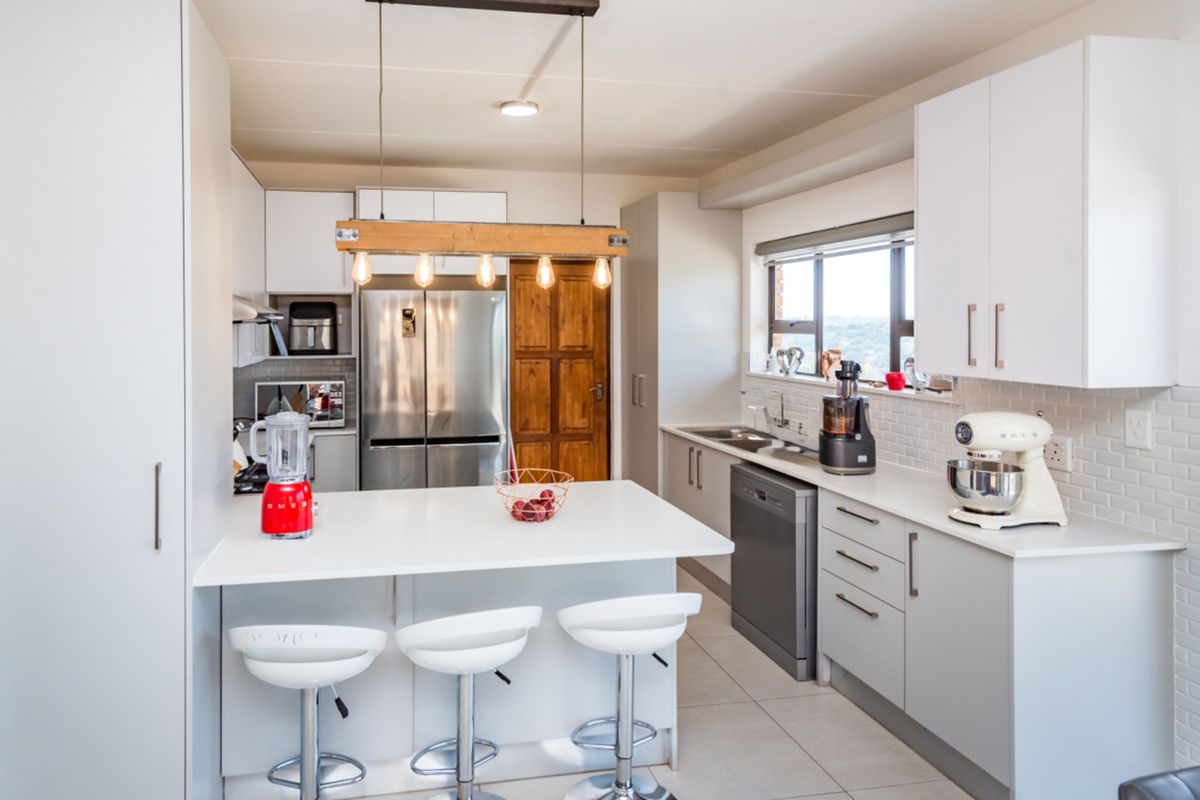 Modern kitchen featuring white cabinetry, quartz countertops, subway tile backsplash, a breakfast bar, and integrated appliances with contemporary pendant lighting.