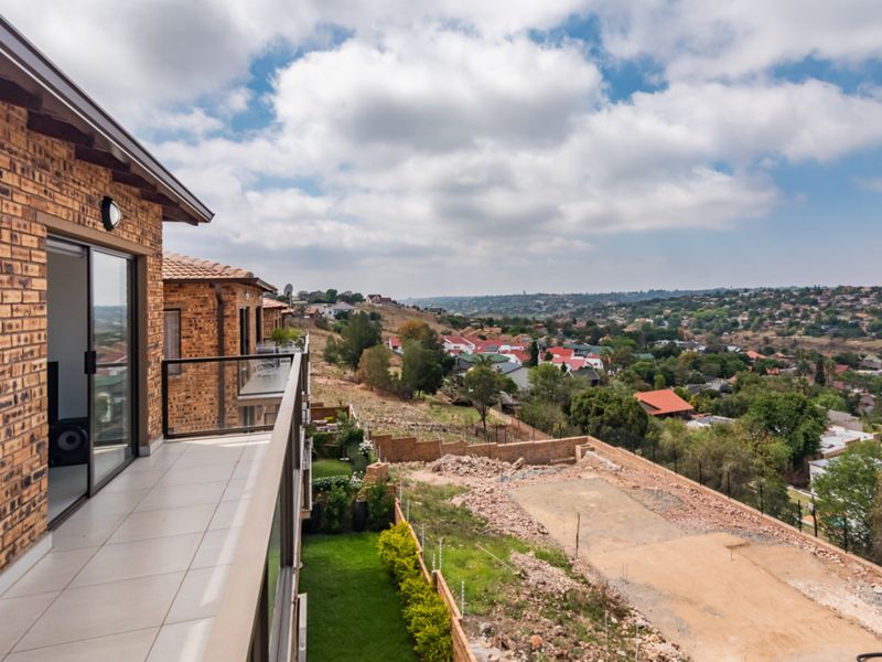 A spacious elevated balcony with tiled flooring and a glass balustrade, offering expansive views over the surrounding residential area.