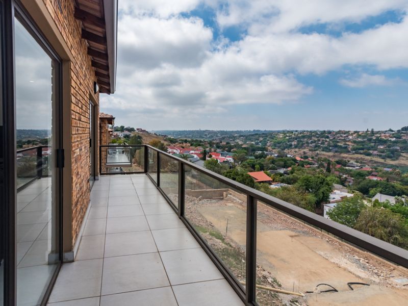 A spacious balcony featuring a modern glass balustrade, tiled flooring, and expansive views over the surrounding residential area.