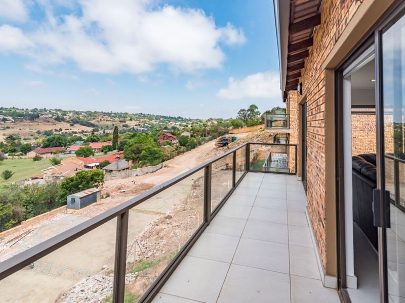 Spacious balcony featuring a modern glass balustrade, tiled flooring, and expansive views over the surrounding residential area.