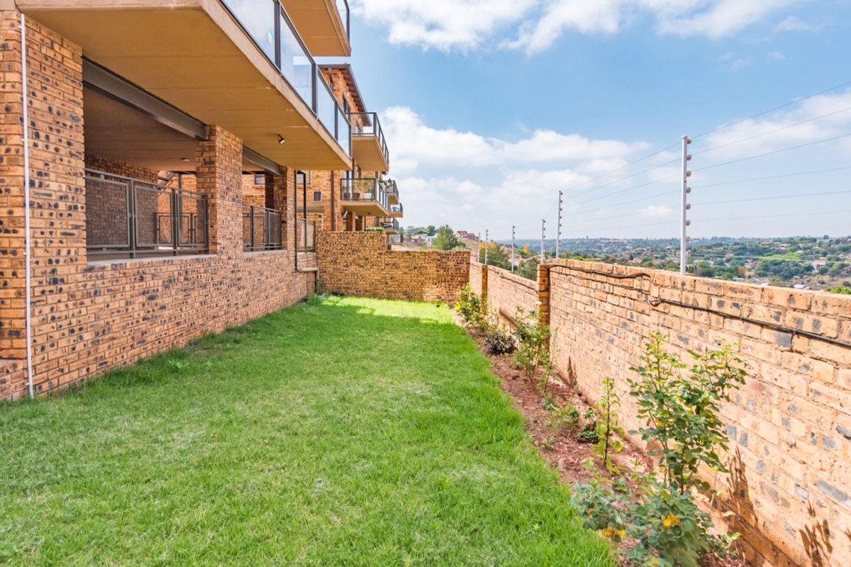 A well-maintained rear garden area featuring a lawn, face brick boundary walls with electric fencing, and an elevated balcony with glass balustrades.