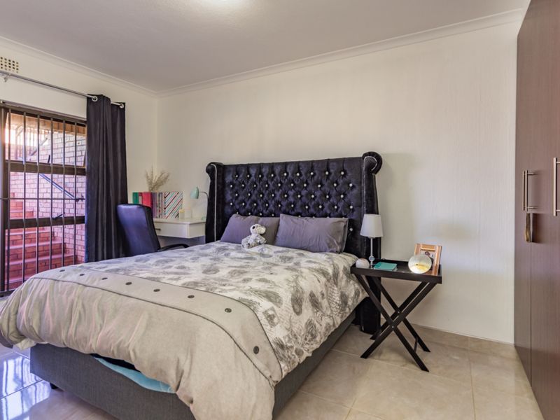 A well-maintained bedroom featuring tiled flooring, a built-in wardrobe, and a sliding door with a security gate providing access to the exterior.