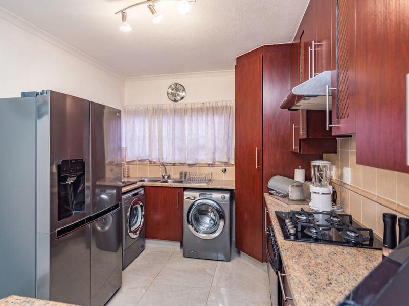 A functional kitchen featuring dark wood cabinetry, granite countertops, a gas hob with extractor, and integrated space for laundry appliances.