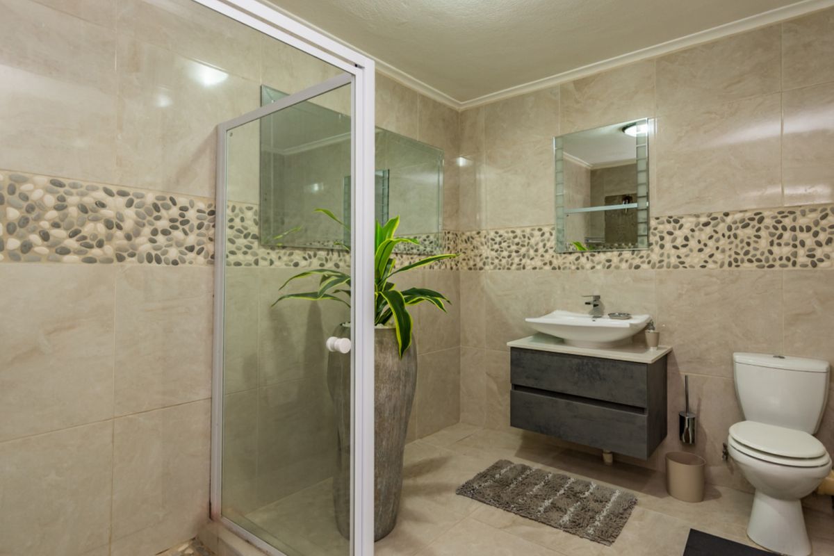 Modern bathroom featuring a glass shower enclosure, wall-mounted vanity with vessel sink, and neutral tiled walls with a decorative pebble border.