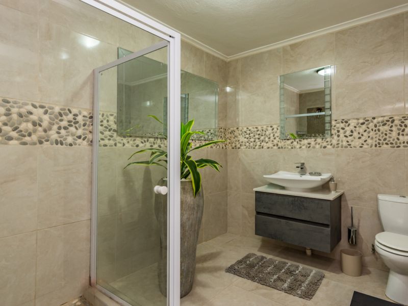 Modern bathroom featuring a glass shower enclosure, wall-mounted vanity with vessel sink, and neutral tiled walls with a decorative pebble border.