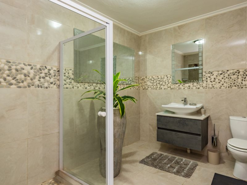 Modern bathroom featuring a glass-enclosed shower, wall-mounted vanity with vessel sink, and neutral ceramic tiling with a decorative pebble accent border.