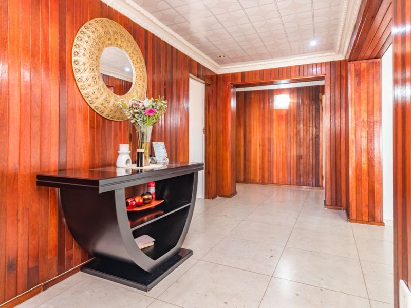 A spacious hallway featuring extensive timber wall paneling, tiled flooring, and decorative ceiling tiles, creating a warm and traditional aesthetic.