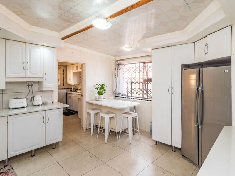 A functional kitchen featuring white cabinetry, tiled flooring, and a drop ceiling, with an adjoining scullery area and security-fitted window.
