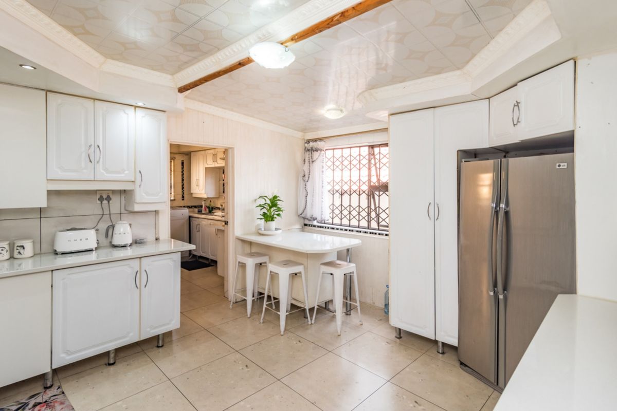 A functional kitchen featuring white cabinetry, tiled flooring, and a drop ceiling, with an adjoining scullery area and security-fitted window.