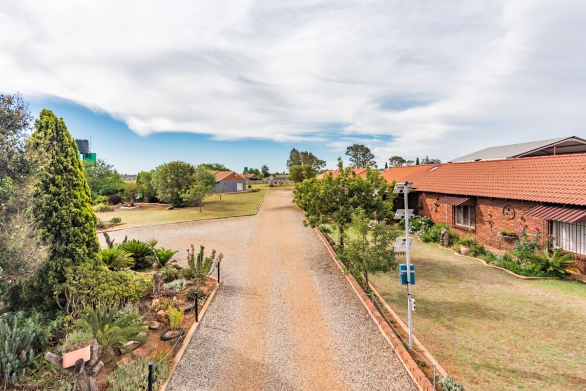 An elevated view of a farm property featuring a long gravel driveway, landscaped gardens, and brick-built structures with terracotta tiled roofs.