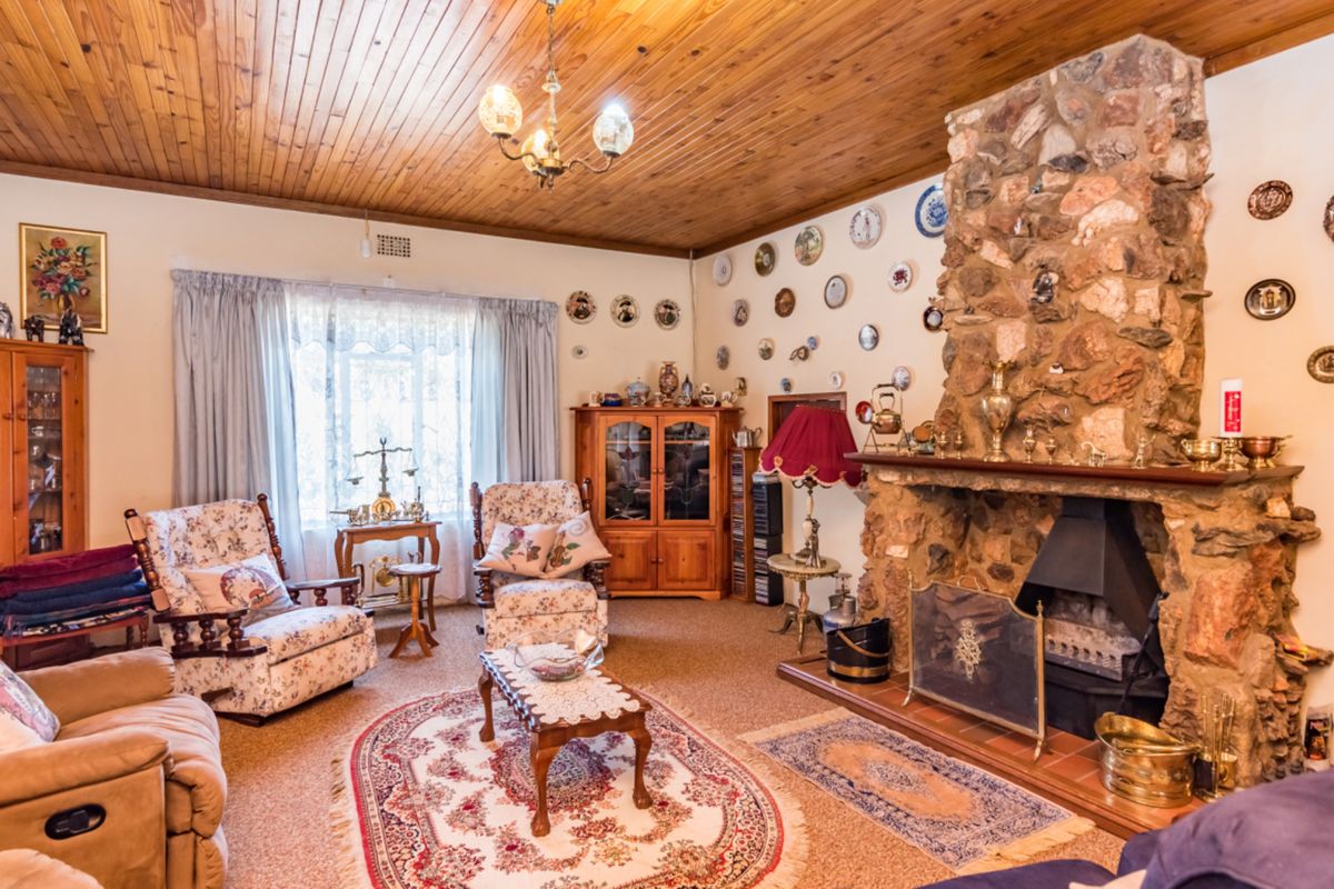 A cozy living room featuring a prominent stone fireplace, wood-paneled ceiling, and large window, offering a traditional and rustic aesthetic.