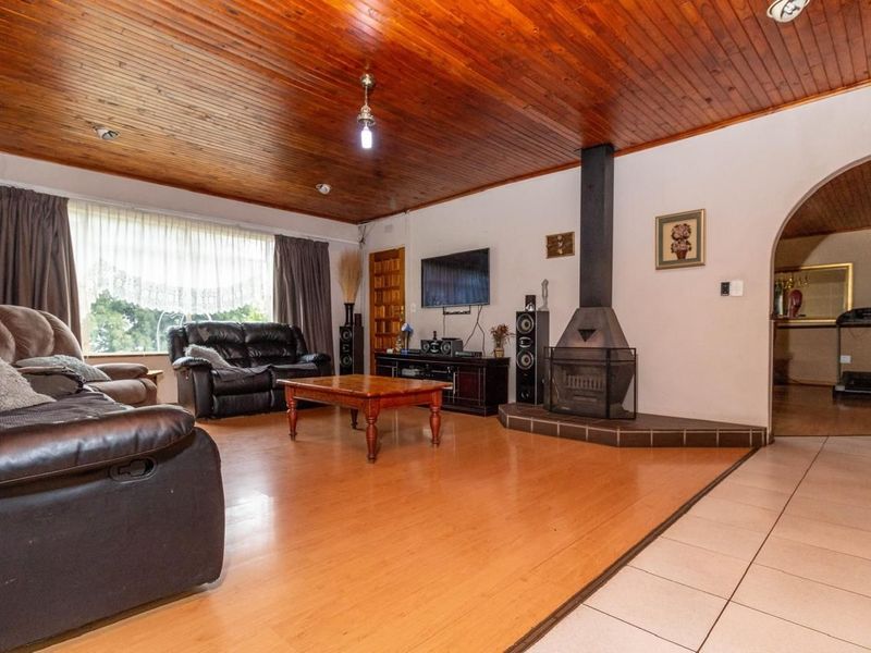 Spacious living room featuring a wood-paneled ceiling, a central freestanding fireplace, and a mix of laminate and tiled flooring with an arched entryway.