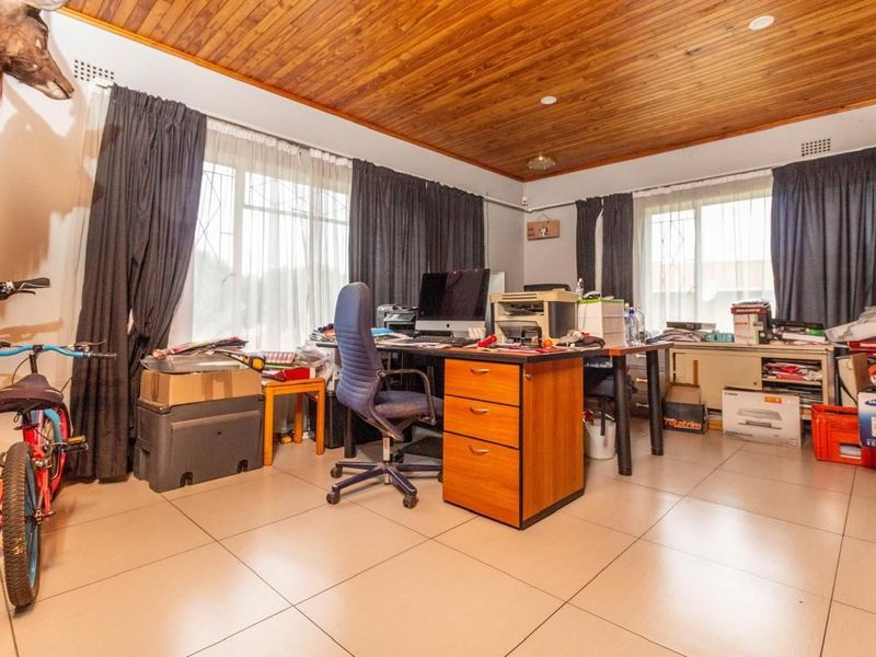 A functional home office space featuring tiled flooring and a classic wooden tongue and groove ceiling with natural light from large windows.