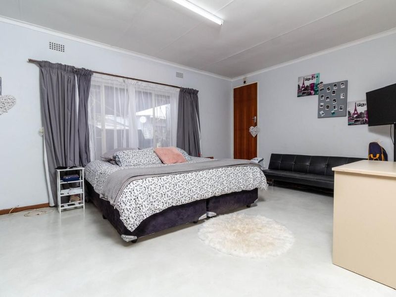 A spacious bedroom featuring neutral walls, tiled flooring, and a large window with curtain fixtures.